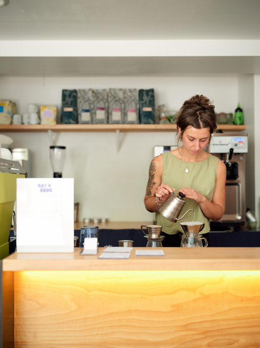 Woman pouring water over coffee filter behind a wooden counter