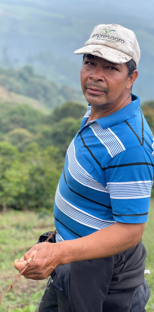 Man wearing a blue striped shirt and cap outdoors with greenery in the background