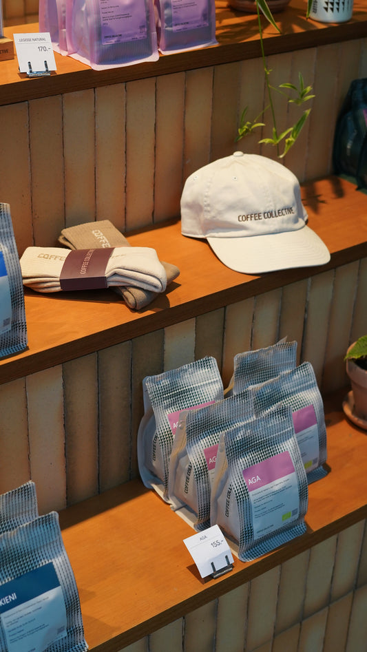 Display of coffee bags and a cap and a pair of socks on a wooden counter with a tiled background.