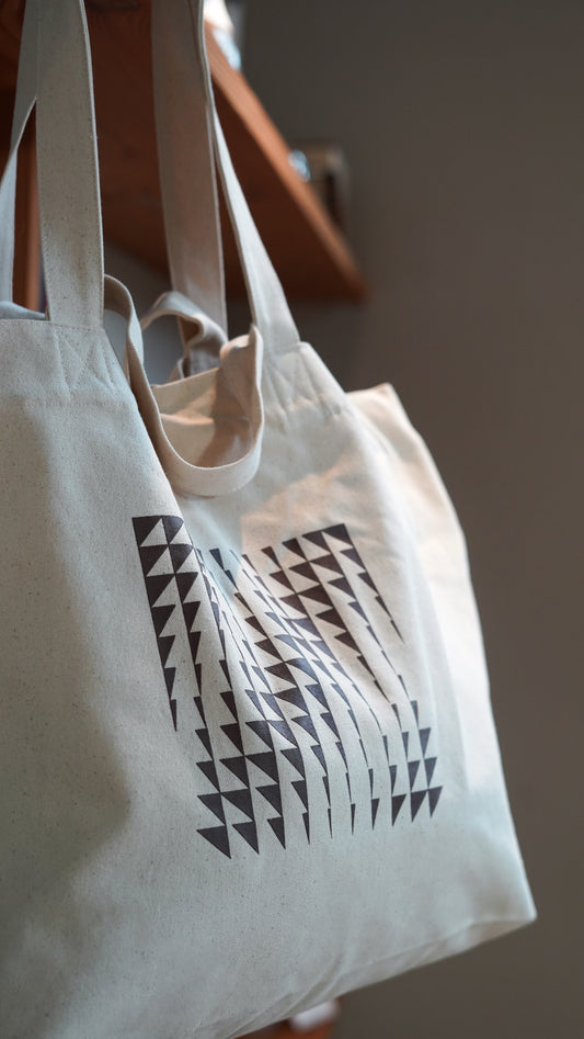 White tote bag with brown geometric pattern hanging from a shelf