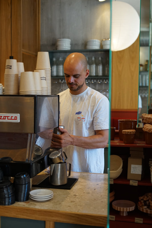 Man steaming milk at espresso machine behind a wooden countertop